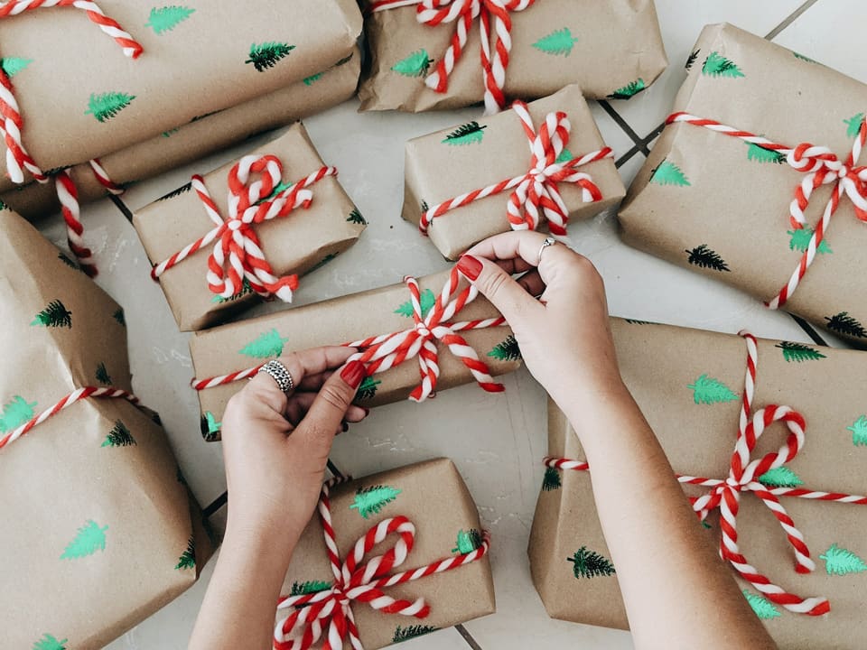 Overhead view of hands tying red-and-white baker's twine around kraft-paper gifts printed with little green trees