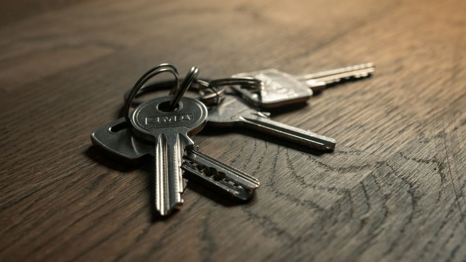 A bunch of house keys on a metal ring lying on a dark wood tabletop in soft light
