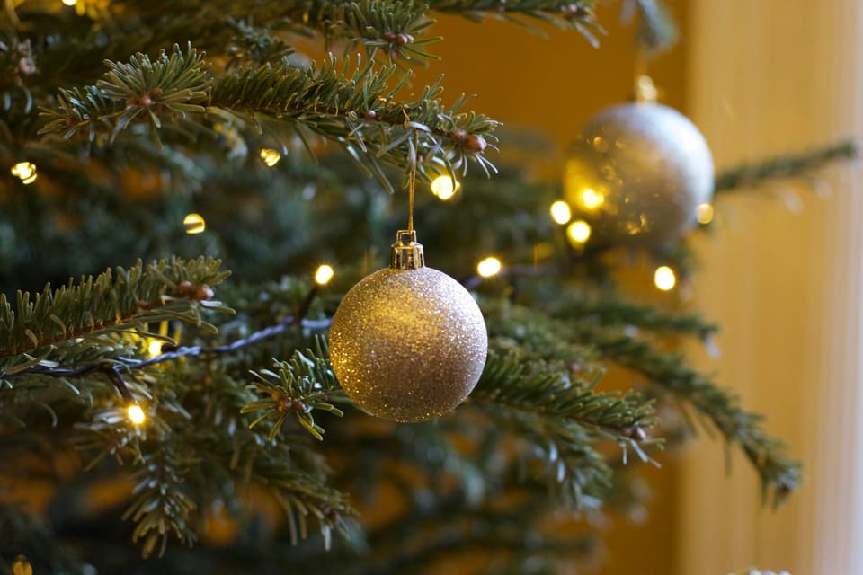 Glittery gold baubles hanging among fir branches and warm fairy lights in a cosy room